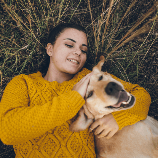 Women laying on the grass with her yellow labrador scratching their head
